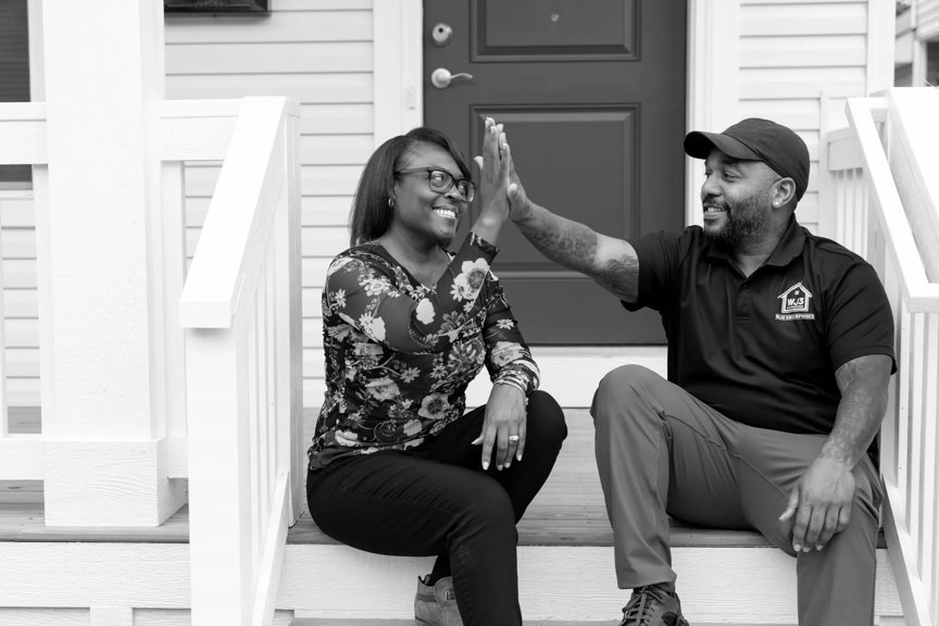 A smiling Sheryl and Wade are seated on front porch steps, giving a high five.