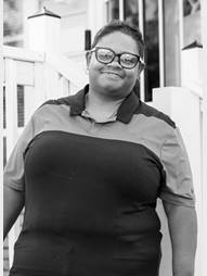 Regina is grinning, standing outside in front of her home.