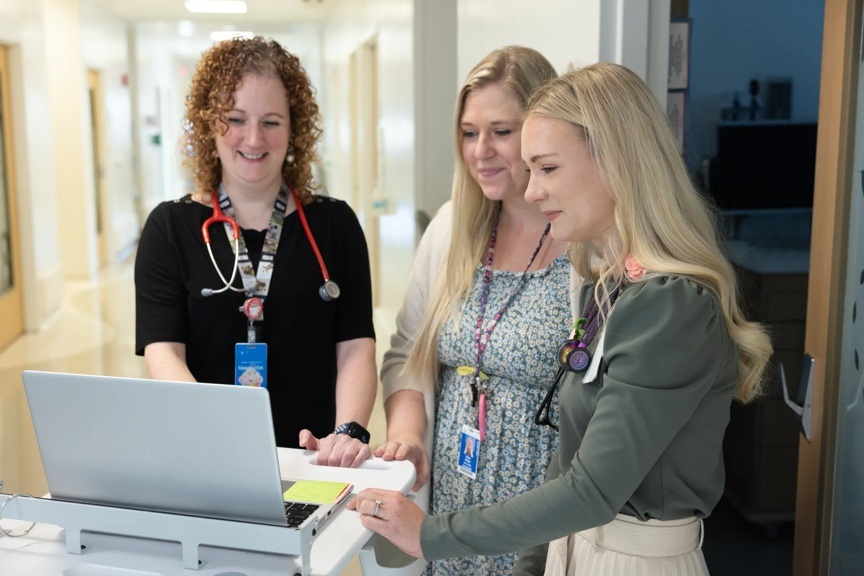 Three providers are standing in a hallway while they gather around a laptop.