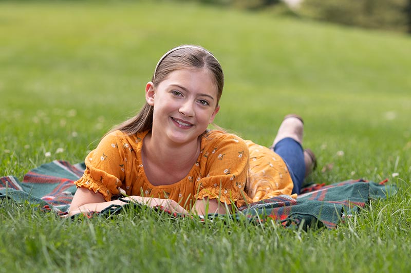a smiling girl laying on a blanket in summertime