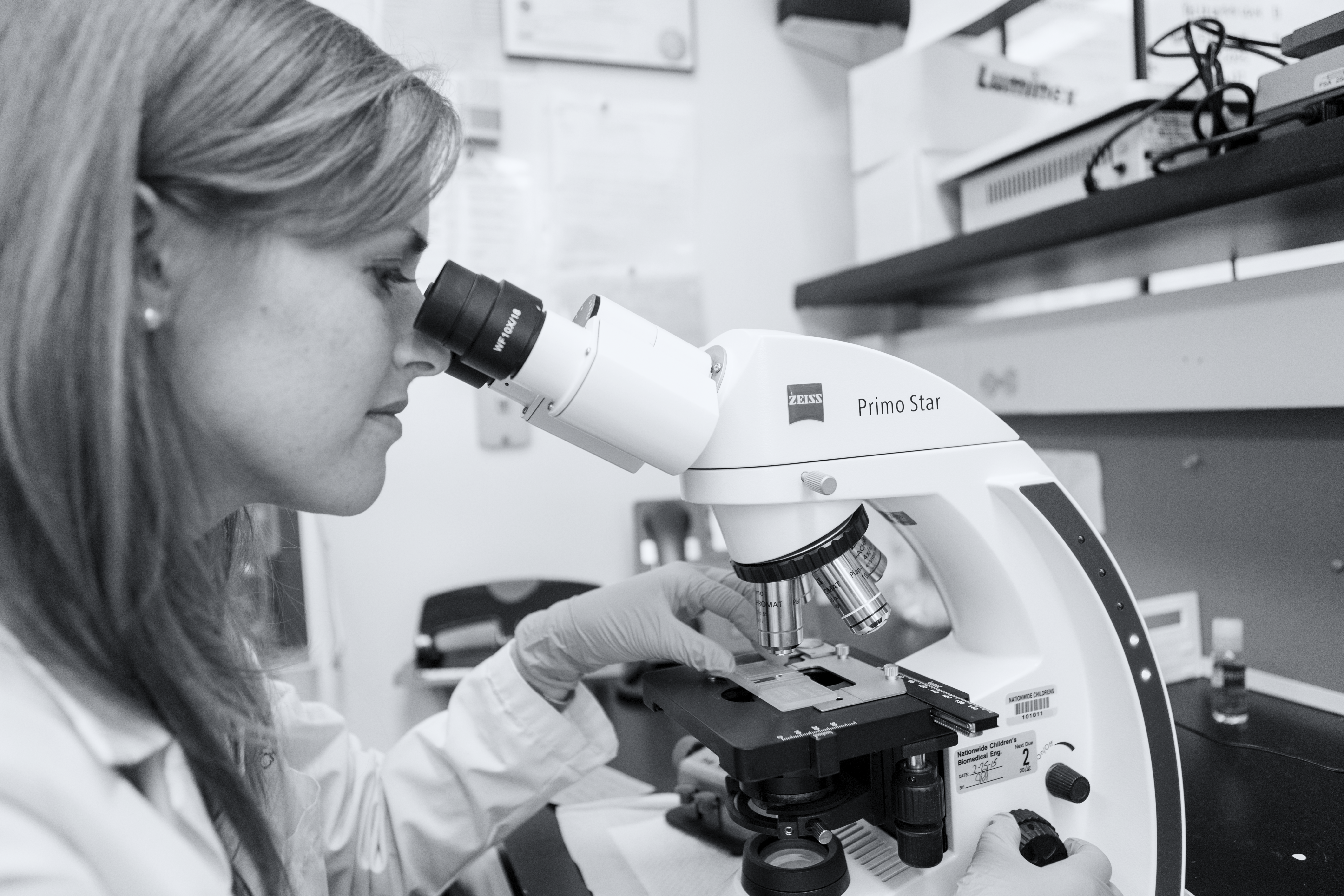 Black and white image of a doctor looking through a microscope. 