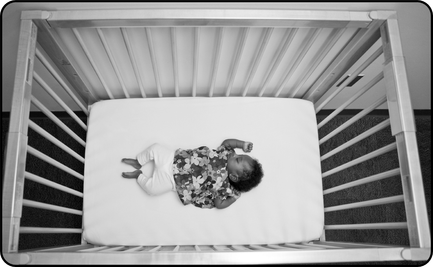 Small baby laying in a crib on their back without a blanket, toys, or pillows.