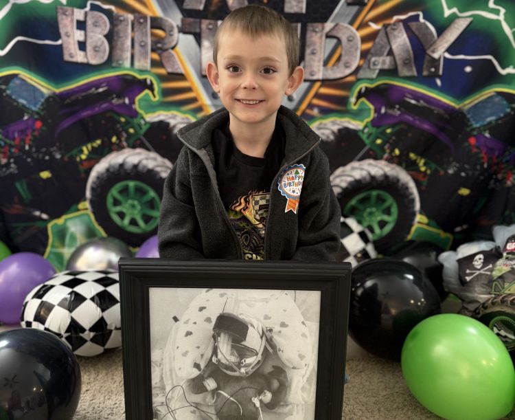 Cooper standing with a picture of him when he was in the NICU