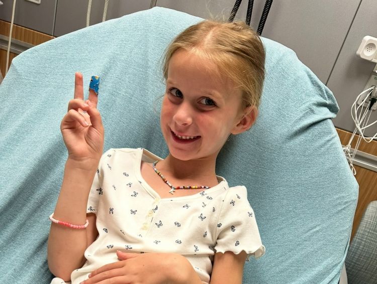 Kennedy in a hospital bed smiling with a peace sign