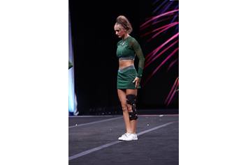 Madi in her green cheer uniform looking down at the mat