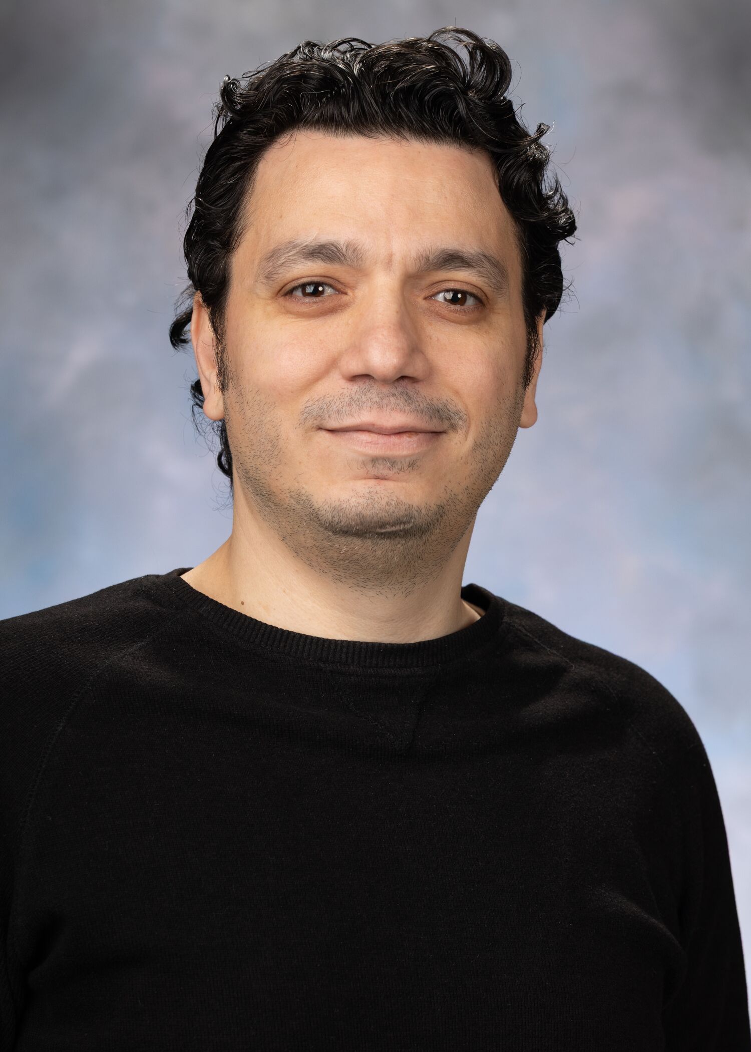 Portrait of Ahmed Kmar. Ahmed had short dark hair and is wearing a black long-sleeved shirt. 