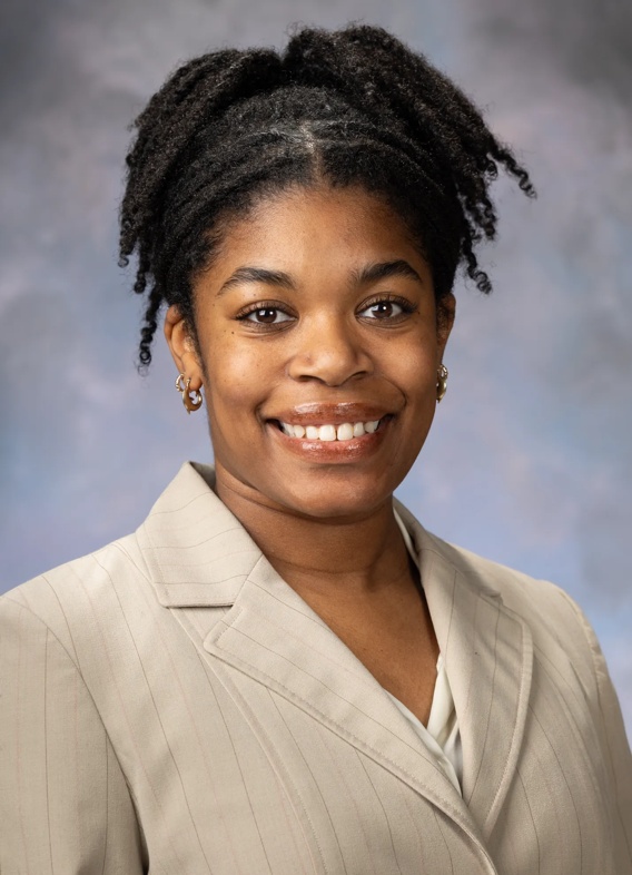 Portrait of Alysha Beard, woman with black hair in a ponytail and a beige blazer.