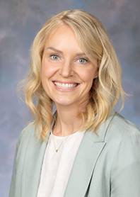 Portrait of Amanda Jensen. Amanda has blonde shoulder length hair and is wearing a white shirt with a sage green jacket.