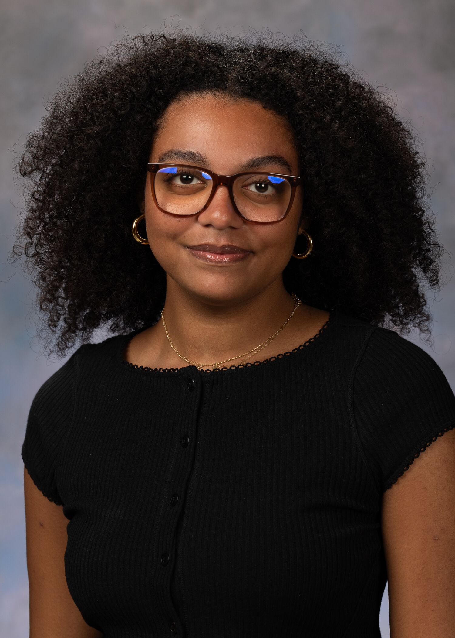 Portrait of Ella Kuffour. Ella has on black square framed glasses and a black t-shirt.