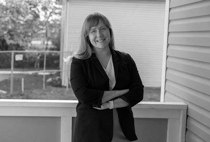 Gretchen West is crossing her arms and smiling. She's standing on a porch at a home in the Linden neighborhood of Columbus, Ohio.