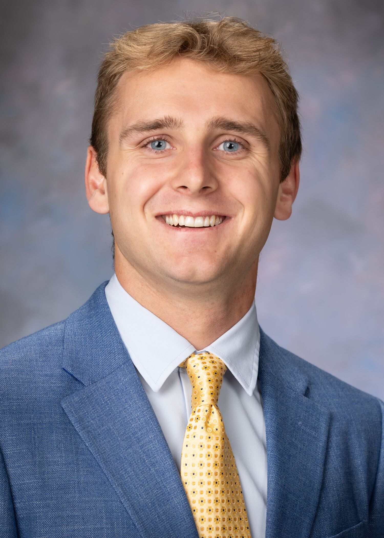 Portrait of Jackson Weeks . Jackson is wearing a navy blue suit jacket with a light blue shirt and gold tie.