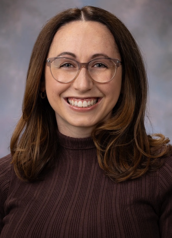 Portrait of Jenna DeCarlo, woman with short brown hair, glasses, and a brown sweater.