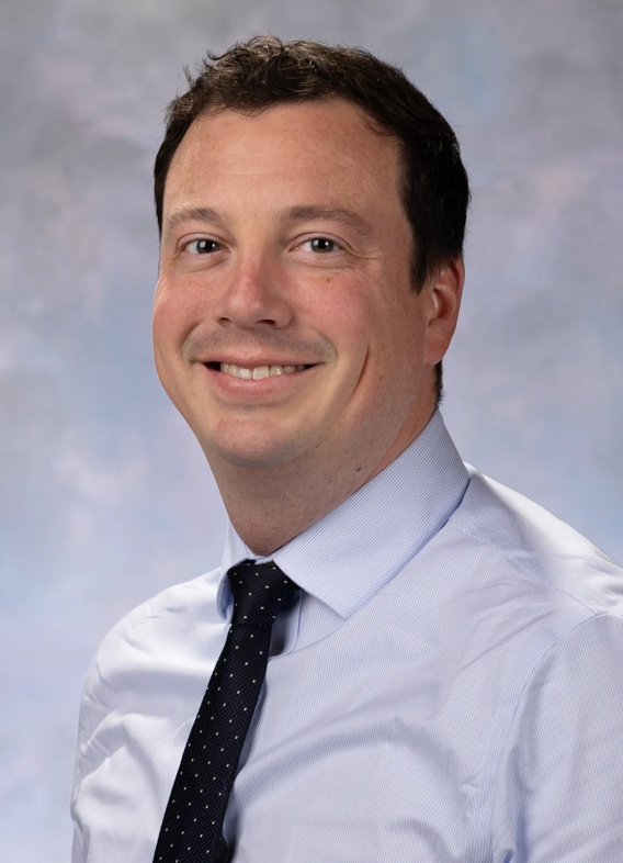 Portrait of Jonathan Medernach. Jonathan is wearing a light-colored button up shirt with a dark colored tie. 