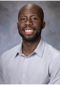 Portrait of Kwasi Minta wearing a light gray dress shirt.
