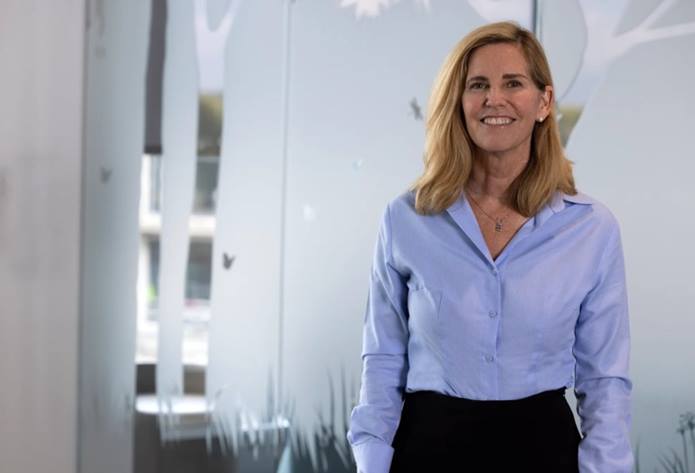 Dr. Glader is wearing a long sleeve, button down shirt. She is smiling and standing in a hallway at Nationwide Children's.