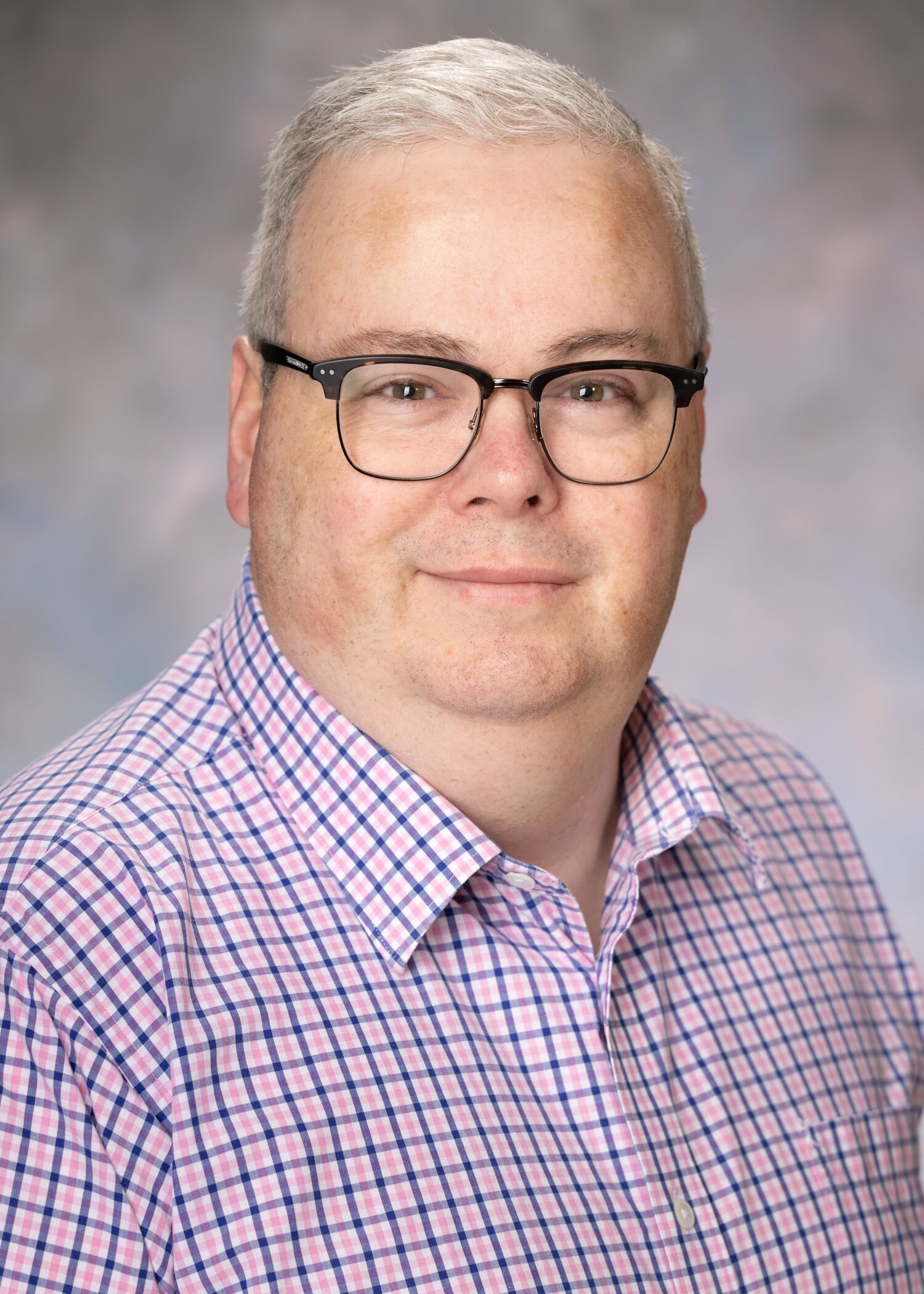 Portrait of Marc Dutro. Marc has short, white hair and glasses. He is wearing a patterned purple and white button-up shirt. 