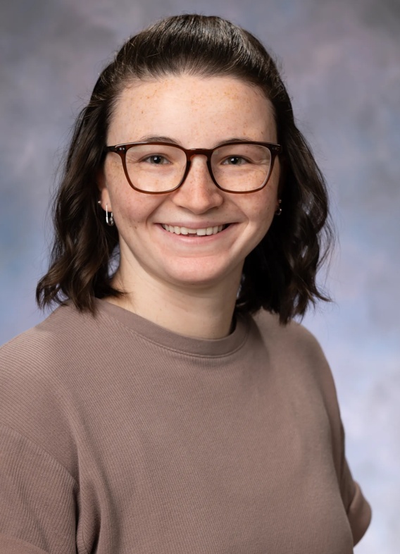 Portrait of Mary Taylor, woman with short brown hair, glasses, and a brown sweater.