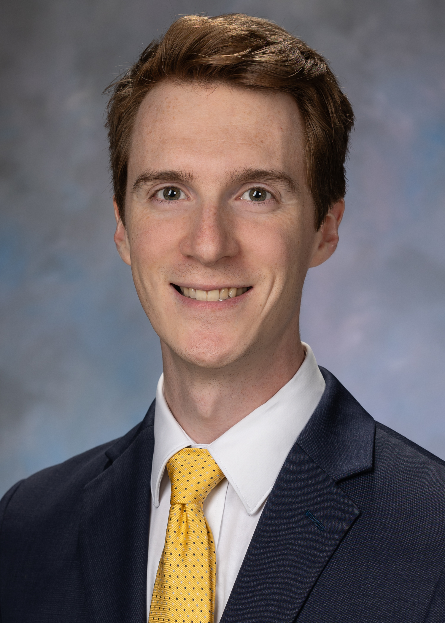 Portrait of McKay Noll. McKay is wearing a black suit jacket, white button up shirt and a yellow tie.