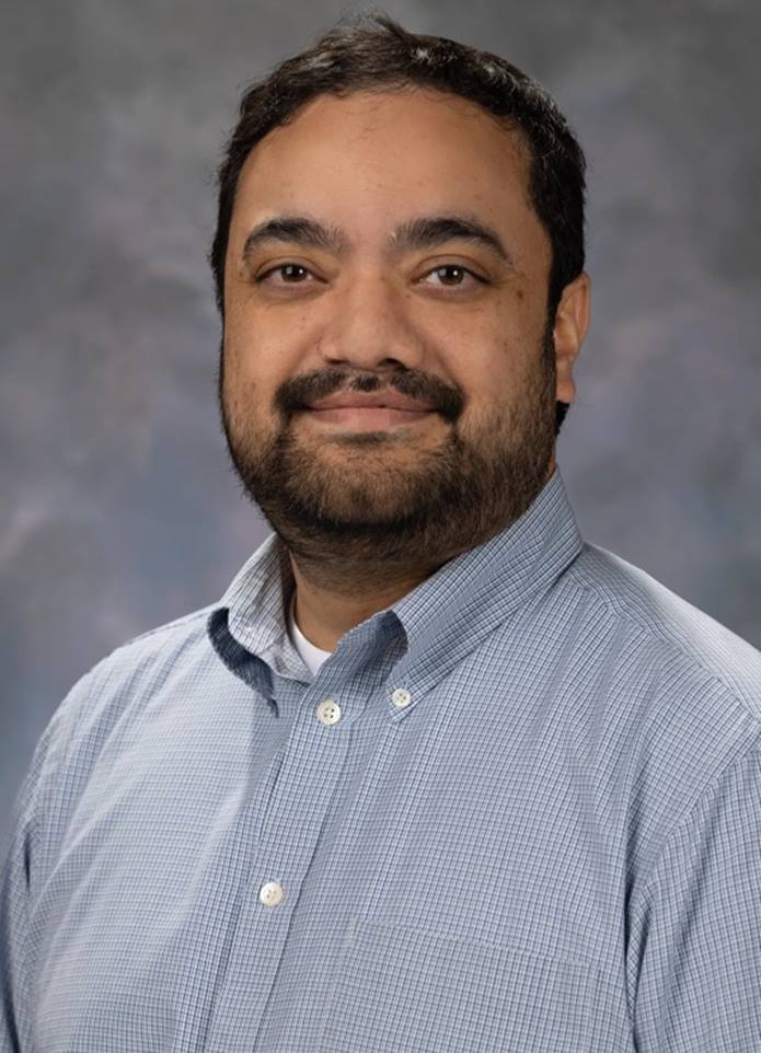 Portrait of Midhat Farooqi, man with short black hair, a beard, and a grey shirt.