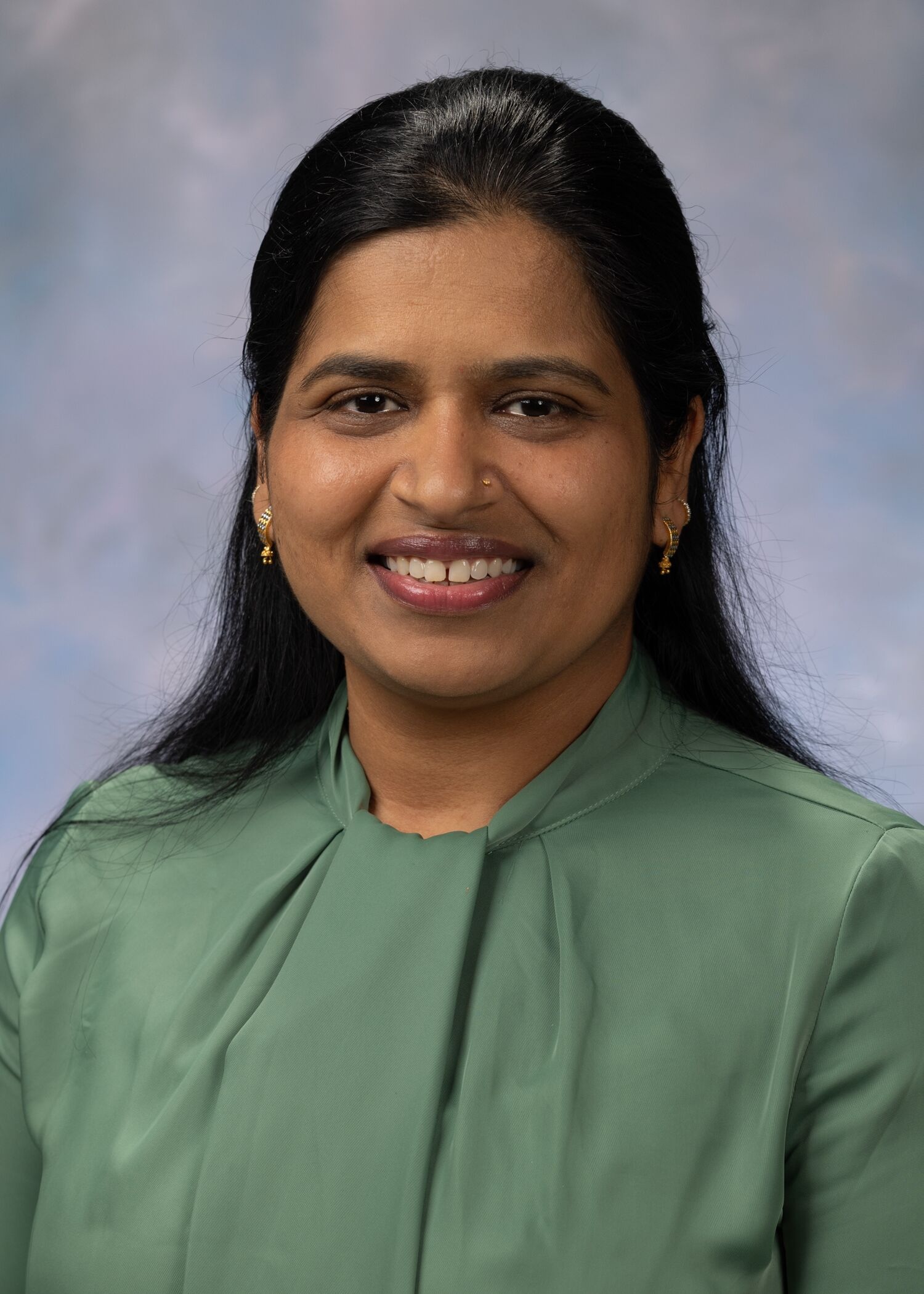 Portrait of Nidhi Chaudhary, PhD. Nidhi has long black hair and is wearing a green top. 
