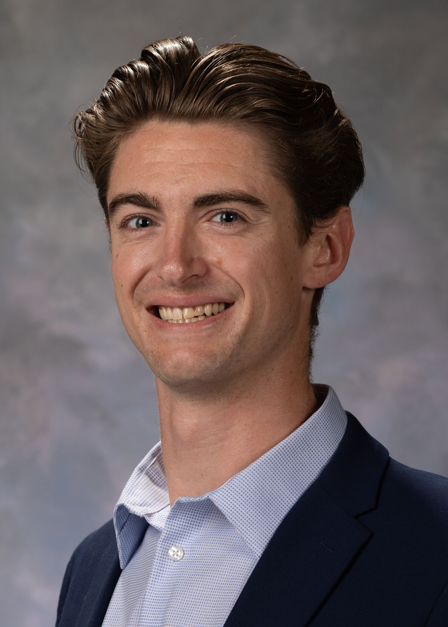 Portrait of Ryan Juncker. Ryan has short brown hair and is wearing a blue button up and a black jacket.