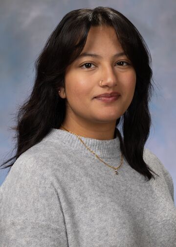 Portrait of Saachi Kuthe. Saachi has long dark hair and is wearing a gray sweater.