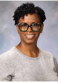 Portrait of Sala Webb. Sala is wearing dark rimmed glasses and a heathered gray top.