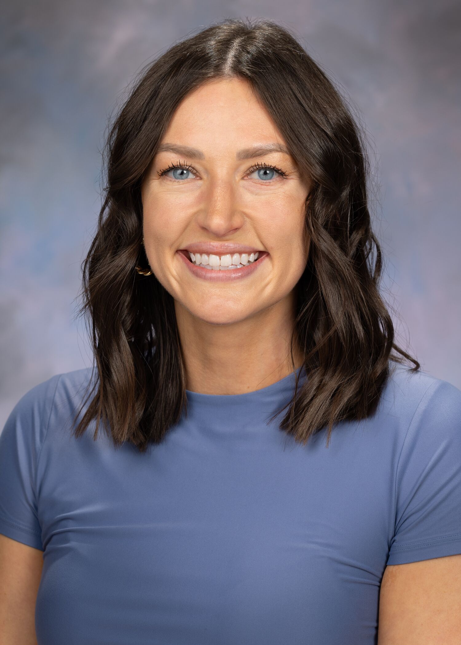 Portrait of Samantha Goedde-Papamihail. Samantha has shoulder-length brown hair and is wearing a short sleeved blue top. 