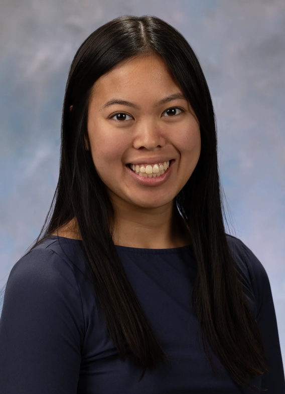 Portrait of Sydney Fojas. Sydney has long dark hair and is wearing a dark colored long sleeved top. 