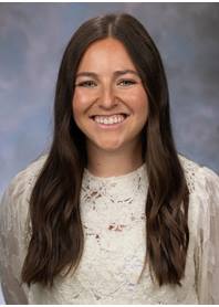 Portrait of Sydney Halliday. Sydney has long dark hair and is wearing a white floral lace top.
