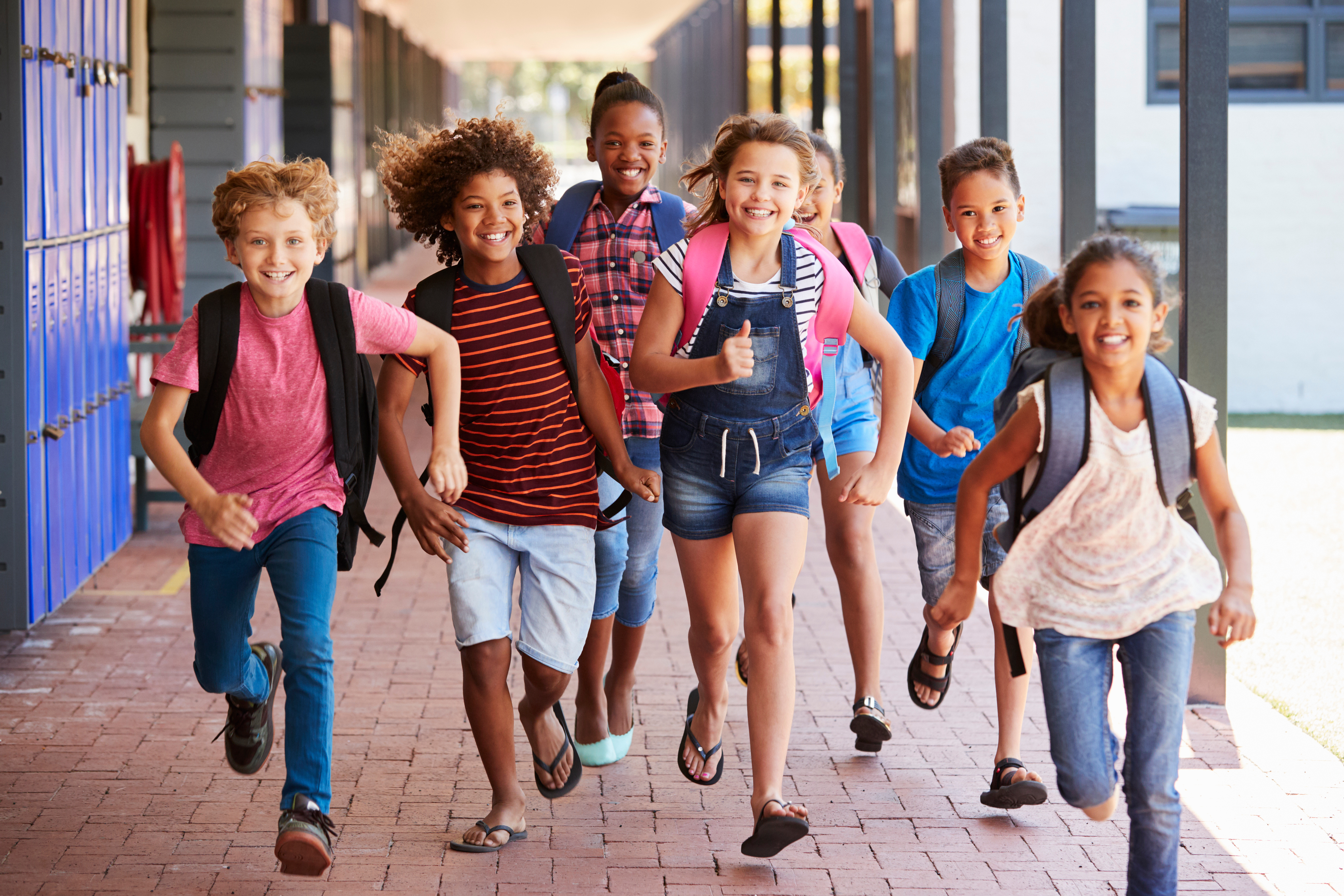 A group of school aged children running and smiling through the hall of a school