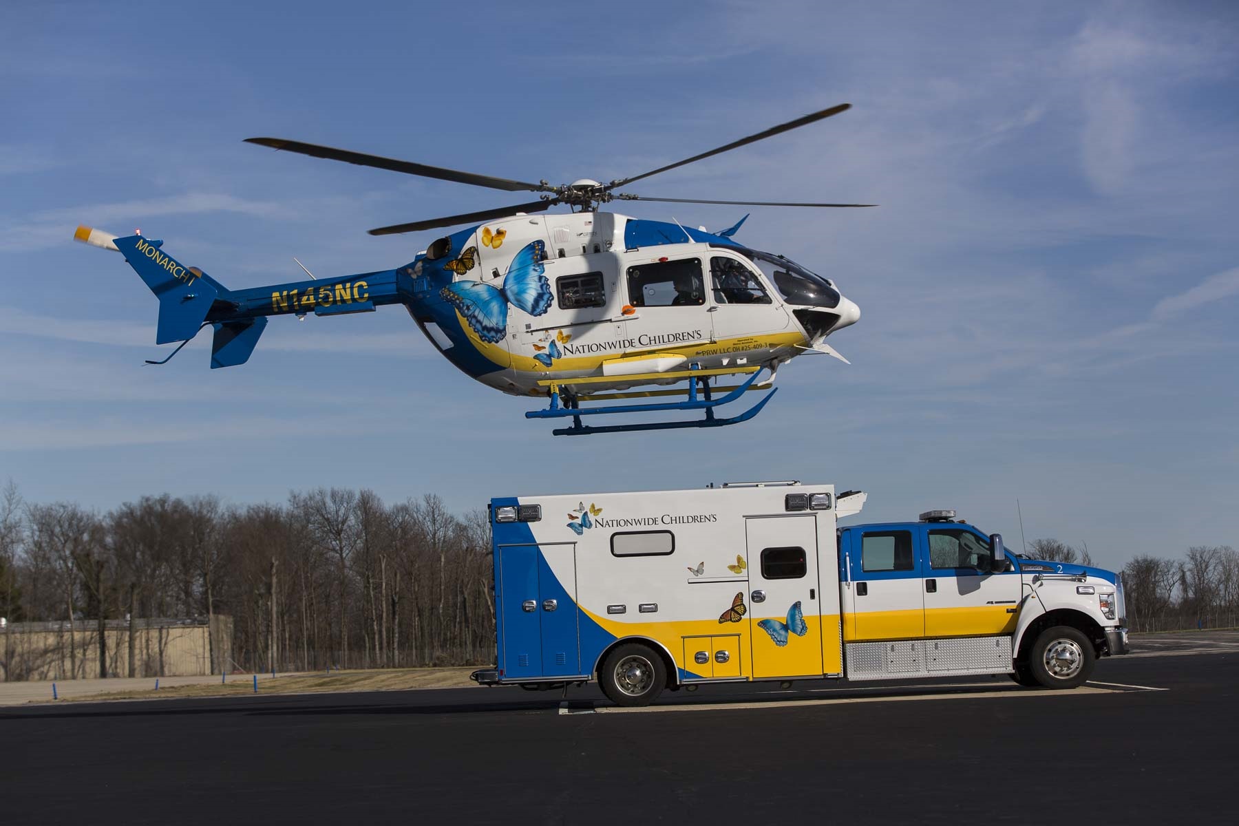 A Nationwide Children's Hospital helicopter and ambulance stand in front of a blue sky and wintery trees.