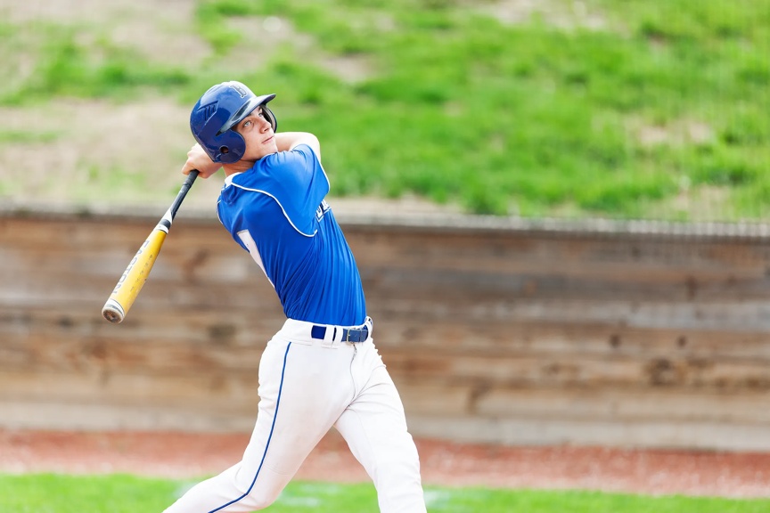 Teen in a blue uniform swinging a baseball bat.