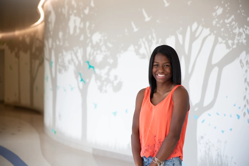 Teenage girl standing in the hospital hallway smiling.