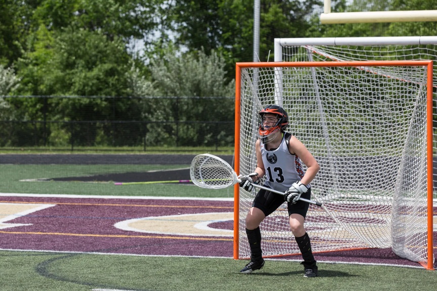 Kid playing lacrosse and standing in the goal.