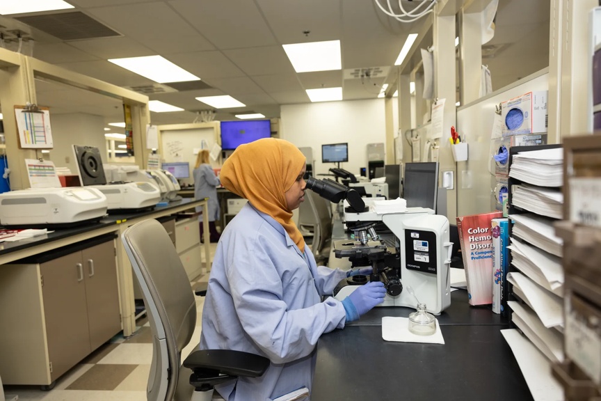 Provider in a lab using a microscope to study samples.