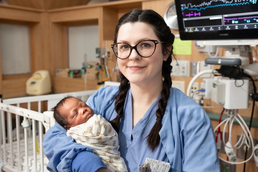 Provider holding an infant swaddled in a blanket.