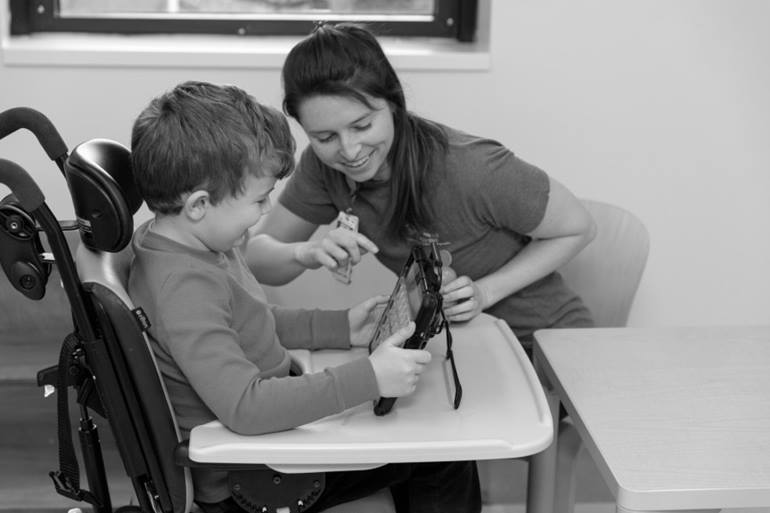 Child in a wheelchair being taught how to use a tablet by a medical professional