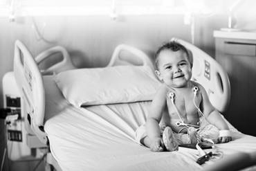 Young child sitting in hospital bed pre or post cardiac procedure.