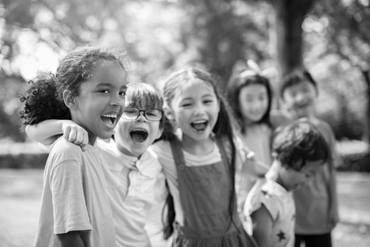 Five children standing with their arms around another smiling.