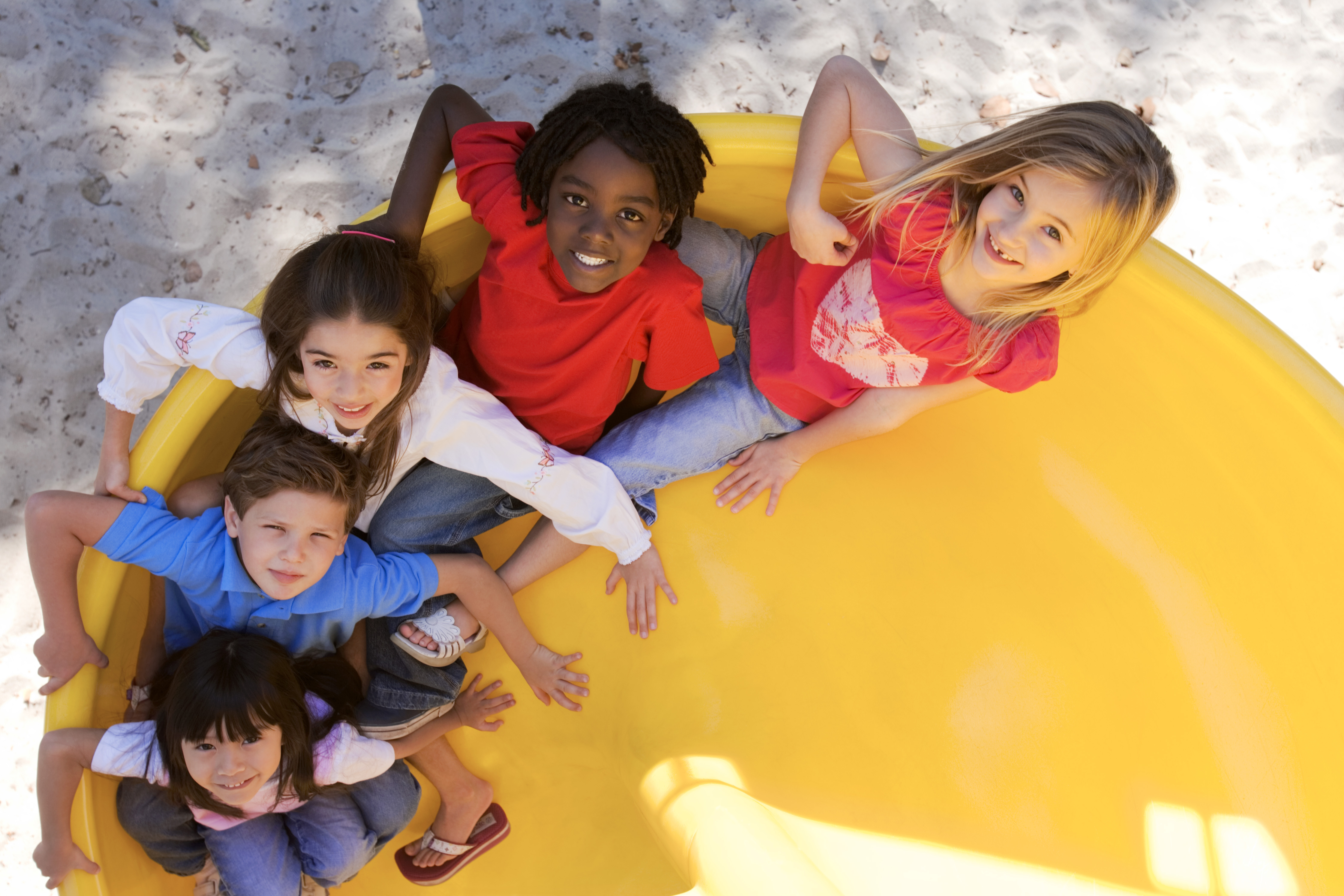 Five children are on a slide sitting behind one another. They are all looking up at the camera and smiling.