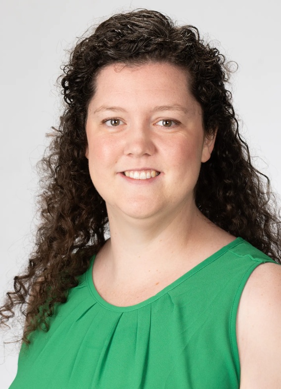 Portrait of Emerald Hanson, woman with long brown hair and a green shirt.