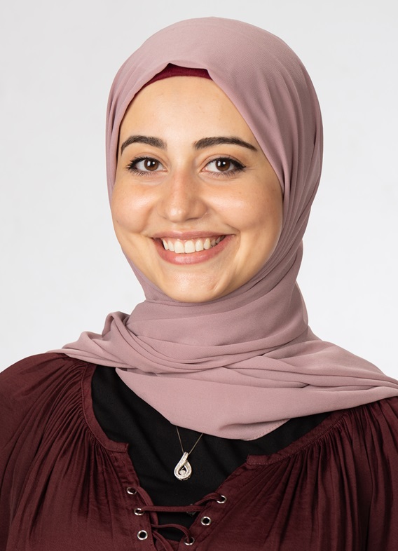 Portrait of May Alarmanazi, woman with a brown head scarf and a striped shirt.