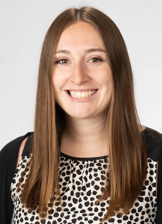 Portrait of Nicole Clayton, woman with long brown hair and a patterned black shirt.