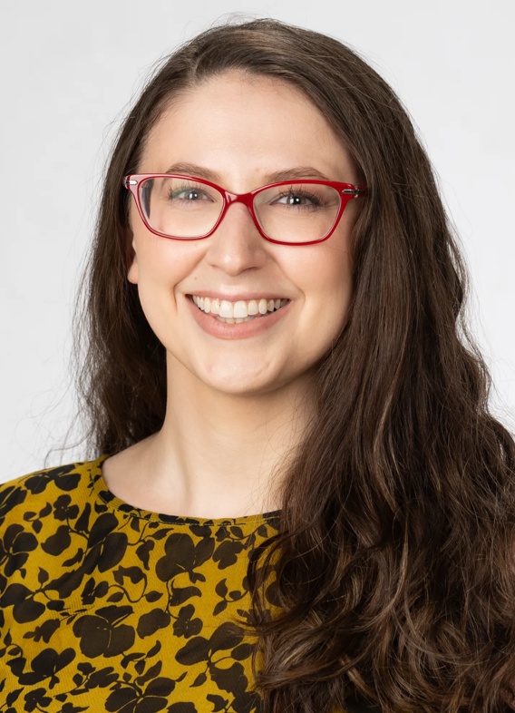 Portrait of Serena Dow, woman with long brown hair, glasses, and a patterned yellow shirt.