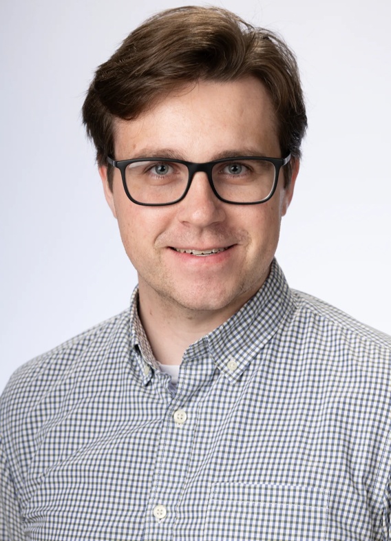 Portrait of Andrew Appert, man with short brown hair, glasses, and a gray shirt.