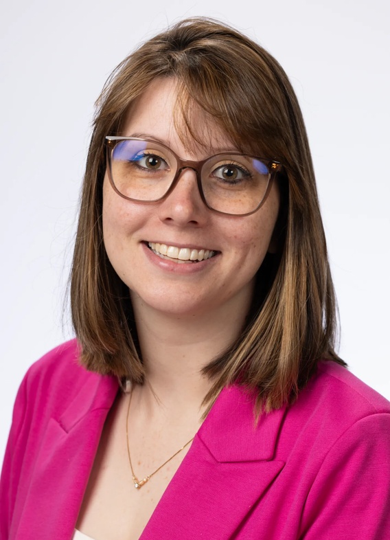 Portrait of Cora Miracle-Poth, woman with short brown hair, glasses, and a pink shirt.