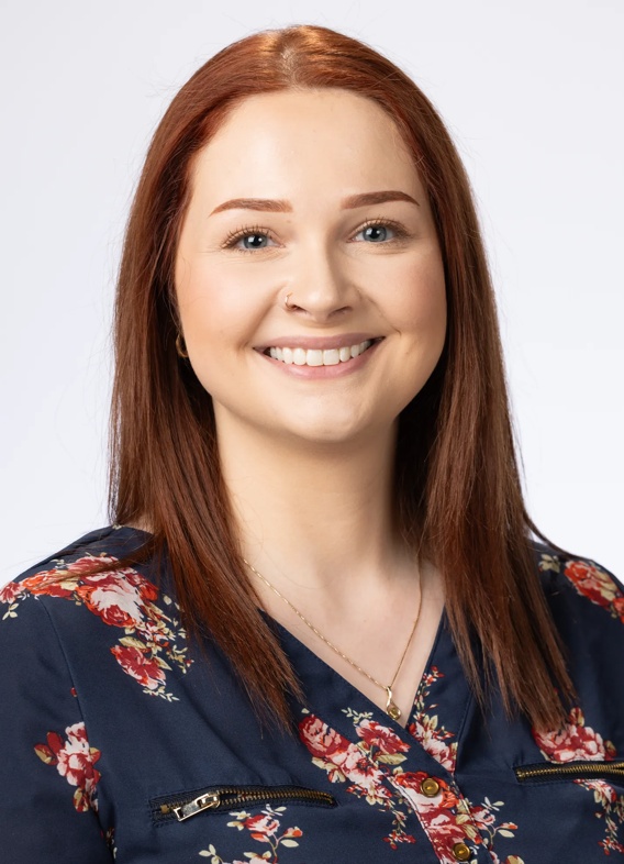 Portrait of Kara Klinkebiel, woman with long red hair and a dark blue floral shirt.