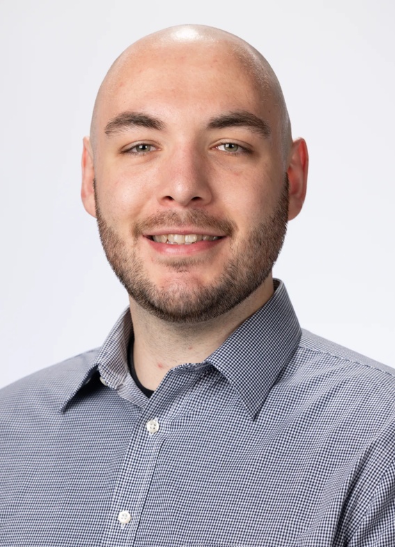 Portrait of Logan Neely, man with a beard and a grey shirt.