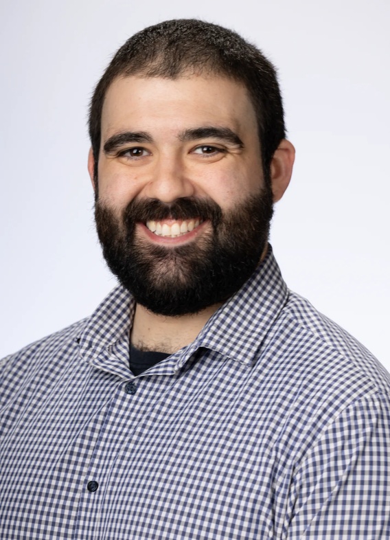 Portrait of Luke Giangregorio, a man with dark brown hair and beard and a grey shirt.